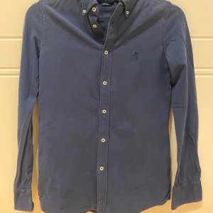 Blå skjorta från Ralph Lauren - Snygg blå skjorta från Ralph Lauren i en klassisk design. Skjortan har långa ärmar och knappar framtill. Perfekt för en stilren look.