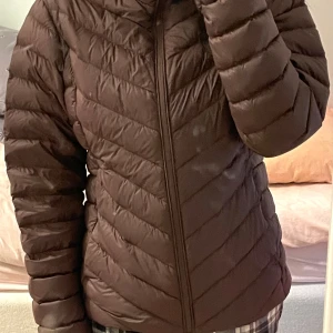 Lila pufferjacka från Mckinley  - Säljer en brun pufferjacka från Mckinley med huva och dragkedja framtill. Jackan har quiltad design med horisontella och sneda sömmar, samt lång ärm. Perfekt för kyliga dagar och enkel att matcha med olika outfits . 