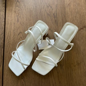 Vita sandaler med klack från H&M - Stilrena vita sandaler från H&M med smala remmar och fyrkantig tå. Skorna har en bred, stabil klack och öppen tå. Klackhöjd ca 9cm. 