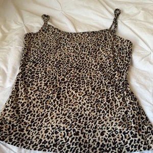 Leopardmönstrad linnetopp med knutband - Säljer en snygg leopardmönstrad linnetopp med smala axelband som är knutna. Toppen har en rak passform och är tillverkad i ett mjukt, lätt material. Perfekt för dig som vill sticka ut med ett djurmönster och cool vibe.