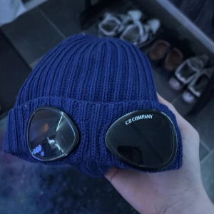 Blå ribbstickad mössa C.P. Company ÄKTA - Säljer en blå ribbstickad mössa från C.P. Company med deras ikoniska goggles framtill. Mössan är i tjockt, stickat material och har uppvikt kant. Perfekt för dig som vill sticka ut med streetwear-vibe och snygga detaljer.