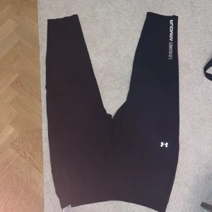 Svarta leggings från Under Armour - Svarta leggings från Under Armour med logga på benet och tryckt text längs sidan. Snygg och sportig design i stretchigt material som passar perfekt till träning. Bekväm passform och klassisk look.