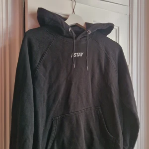 Svart hoodie från Stay med huva - Svart hoodie från Stay med broderad logga på bröstet. Klassisk modell med stor huva, snörning och känguruficka framtill. Tillverkad i mjuk bomullsmix. 