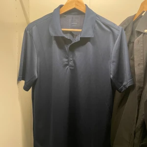 Golf pike från adidas aldrig använd. - Snygg mörkblå pikétröja från Adidas med klassisk krage och två knappar framtill. Tröjan har korta ärmar och en vit Adidas-logga på ena ärmen. Perfekt för en sportig och stilren look.