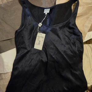 Sidenlinnetopp Armani - Äkta svart linnetopp från Armani Collezioni i sidenmaterial. Toppen har v-ringning och ärmlös design. Helt oanvänd och prislappen sitter fortfarande på