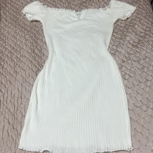 Vit ribbad offshoulder kortklänning - Supersöt vit kortklänning med ribbad struktur och offshoulder-modell. Klänningen har en liten v-ringning framtill och smala ärmar. Perfekt för sommarens alla tillfällen och ger en fräsch och trendig look.
