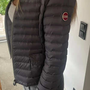 Grå dunjacka från Colmar - Snygg grå dunjacka från Colmar med quiltad design och rund halsringning. Jackan har dragkedja framtill, två fickor och ett diskret Colmar-märke på ärmen. Perfekt för dig som vill ha en lätt och stilren jacka med figursydd passform. Har en liten fettfläck på ryggen som knappt syns(bild 4) men annars i jättefint skick!! Strl XS/S