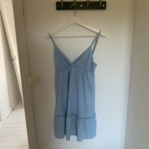 Blåvit randig sommarklänning HM S - Supersöt blå och vit randig klänning från HM i storlek S. Klänningen har smala axelband, v-ringning och volang nertill. Perfekt för varma dagar med sitt lätta tyg och avslappnade passform.