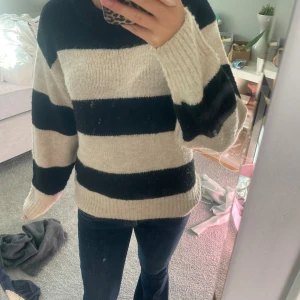 Randig stickad tröja i svart och beige - Säljer en mysig stickad tröja med breda svarta och beige ränder. Tröjan har rund hals, långa ärmar och en relaxed fit. Perfekt för att hålla sig varm och snygg under kyliga dagar.