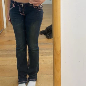 Mörkblå jeans med rosa sömmar - Snygga mörkblå jeans med kontrasterande rosa sömmar och klassisk femficksdesign. Byxorna har låg midja och raka ben, perfekt för en trendig och avslappnad look. Passar dig som gillar detaljer och vill sticka ut lite extra.