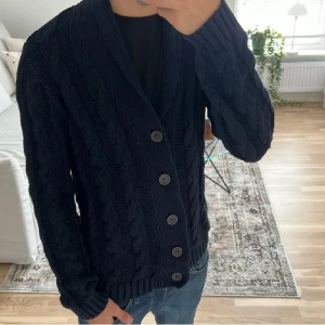 Mörkblå kofta Selected Homme - Säljer en mörkblå kofta från Selected Homme. Koftan har grovstickat mönster, bred sjalkrage och knäpps med fem stora knappar framtill. 