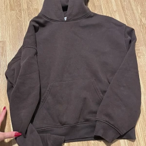 Mörkbrun hoodie med huva - En stilren mörkbrun hoodie med huva och magficka. Tröjan har långa ärmar, ribbade muddar och en klassisk passform. Perfekt för dig som gillar en enkel och clean look.