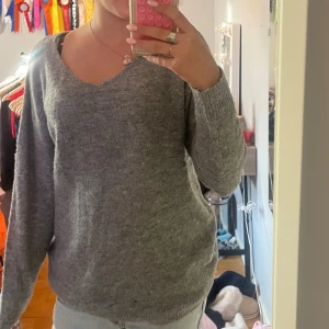 Grå stickad tröja från 157, v-ringad - Mysig grå stickad tröja från 157 med v-ringning och långa ärmar. Tröjan har en avslappnad passform och ribbade muddar vid ärmslut och nederkant. Perfekt för lager-på-lager under kyliga dagar.