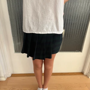 Mörkgrön och svart plisserad kjol Zara - Säljer en kort plisserad kjol från Zara Basic i mörkgrönt och svart randigt mönster. Kjolen har en klassisk A-linjeform och sitter snyggt i midjan. Perfekt för dig som gillar preppy stil och vill ha något som sticker ut lite extra. Shorts under och på baksidan. 