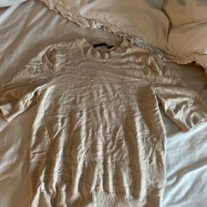 Beige stickad tröja från 157 XS - Beige stickad tröja från 157 i storlek XS. Tröjan har rund halsringning, ribbade muddar och trekvartsärm. Enkel och stilren modell som passar perfekt till lager-på-lager under hösten eller våren.