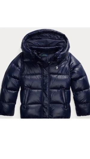 Mörkblå pufferjacka från Polo Ralph Lauren - Snygg mörkblå pufferjacka från Polo Ralph Lauren med glansig finish och klassisk logga på bröstet. Jackan har huva, dragkedja och är vadderad för extra värme. Perfekt för kalla dagar när du vill hålla stilen.