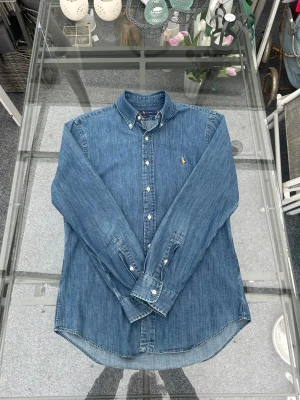 Ralph Lauren denimskjorta Slim Fit M – klassisk jeansskjorta - Snygg Ralph Lauren denimskjorta i Slim Fit, storlek M. Mjuk och perfekt tvättad denim som ger en tidlös och clean look. Klassisk button-down-krage och broderad logo. Skjortan är i fint skick utan fläckar eller defekter. Passar både som vardaglig jeansskjorta och för en mer stilren outfit – ett riktigt kvalitetsp­lagg som håller länge. 