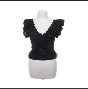 Svart croppad blus med volang - Säljer en svart blus med djup v-ringning och volangdetaljer längs halsen och axlarna. 🤍från Nelly 