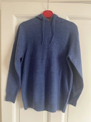 Blå stickad kashmir/merino hoodie med huva - Mysig blå hoodie med huva och snörning, stickad i mjukt material. Tröjan har långärmade och en relaxed passform som gör den skön att bära. Passar dig som är 177 lång, Str m/s. Skriv gärna om ni har frågor!