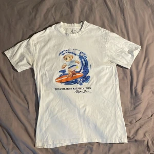 Vit Polo Bear t-shirt från Ralph Lauren - Säljer Vit t-shirt från Ralph Lauren med Polo Bear-tryck, eftersom den blivit för liten . Modellen är slim fit och har korta ärmar. Materialet är mjuk bomull. Perfekt för dig som gillar en stilren och clean look. Pris går att diskuteras