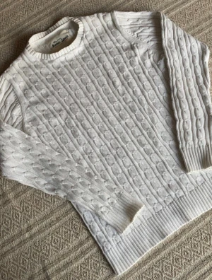 Kabelstickad tröja - Säljer en vit stickad tröja från Iconic Sport i storlek small. Tröjan har ett klassiskt kabelstickat mönster, rund hals och ribbade muddar vid ärmslut och nederkant. Perfekt för dig som gillar stilrena och mysiga plagg med lite preppy vibe.