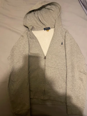 Grå hoodie från Polo Ralph Lauren - Grå hoodie från Polo Ralph Lauren med klassisk blå broderad logga på bröstet. L i barnstorlek vilket motsvarar ungefär xs i herr.