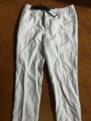 Ljusbeige linnebyxor från Junk de Luxe  - Helt ny. Jag fick de som present de va lite står för mig .Snygga ljusbeige linnebyxor från Junk de Luxe i storlek 52. Byxorna har elastisk midja, raka ben och bakfickor med knapp och dragkedja. Perfekta för en chill och stilren look under varmare dagar.