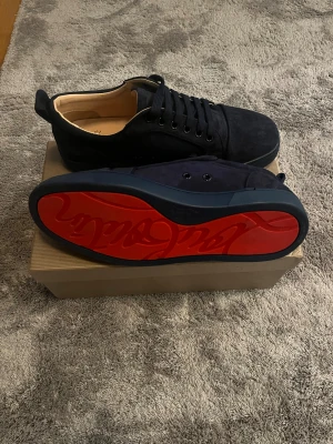 Christian Louboutin mörkblåa sneakers mocka - Snygga svarta sneakers från Christian Louboutin i mocka med klassisk röd sula och diskret logga undertill. Skorna har rund tå, platt sula och svarta snören. Perfekta för dig som vill ha en lyxig och stilren look med en touch av Paris. Skriv dm för mer info. Passar för dom som har 42-43 i storlek. Aldrig använda