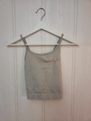 Beige ribbad linnetopp från Gavelo - Säljer en beige ribbad linnetopp från Gavelo med tunna axelband som korsas i ryggen. Toppen har en croppad passform och diskret logga framtill. Aldrig använd! Djur finns i hemmet.