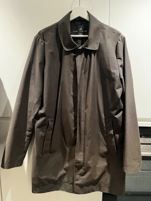 Mörkgrön rock från UBR - Snygg mörkgrön rock från UBER Oslo Norway med minimalistisk design, klassisk krage och dolda fickor. Jackan har dragkedja och knappstängning, är tillverkad i ett lätt och tekniskt material med stormskydd och reflekterande detaljer. Perfekt för dig som gillar stilren och funktionell ytterjacka. OBS liten i storleken.