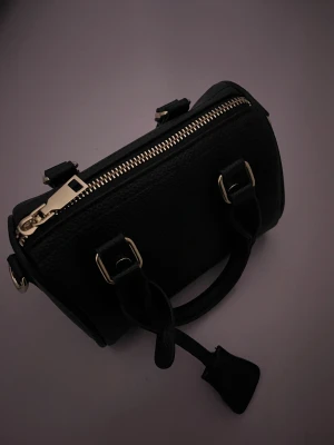 Svart handväska med guld detalj  - Svart handväska med guld detaljer. Liten men rymlig. Har ett tillhörande axelband som följer med 