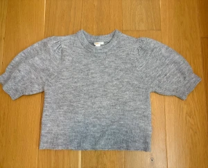 Grå stickad tröja med puffärm Gina Tricot - Supermysig grå stickad tröja från Gina Tricot med puffiga korta ärmar och ribbad kant vid hals, ärmslut och nederkant. Perfekt för dig som gillar en chill och trendig look. Passar dig som vill ha något mjukt och snyggt till hösten eller vintern.