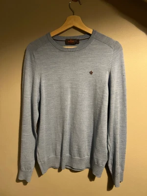 Ljusblå merinoulltröja från Morris - Snygg ljusblå stickad tröja från Morris i 100% merinoull. Rund halsringning, diskret Morris-logga broderad på bröstet och ribbade muddar vid ärmslut och nederkant. Perfekt för dig som gillar stilrena och mjuka plagg.