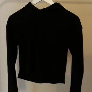 Svart croppad hoodie med huva - Svart croppad hoodie med lång ärm och huva. Enkel och stilren design utan synliga detaljer eller mönster. 