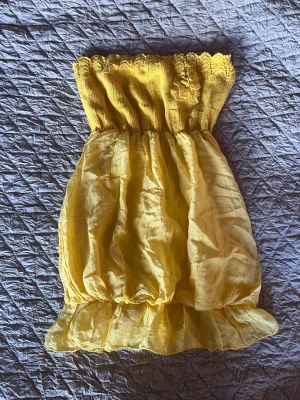 Gul axelbandslös top - Superfin gul axelbandslös top med stickad överdel och volangkant nedtill. Överdelen är ribbad och har en söt blomdetalj. 