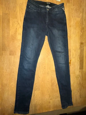 Mörkblå skinny jeans från Replay - Snygga mörkblå skinny jeans från Replay med klassisk femficksdesign och diskreta slitningar. Jeansen har normal midja och raka bakfickor med Replay-logga. Tillverkade i stretchig bomullsblandning för en bekväm passform. Hör av er om ni har några frågor.