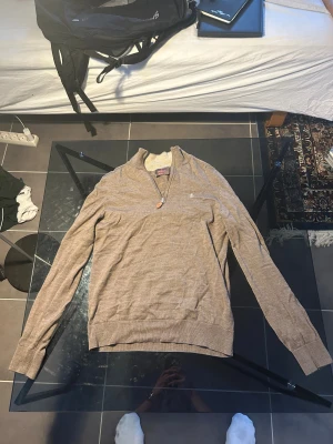 Beige half zip tröja från Morris - Snygg beige långärmad tröja från Morris i 100% merinoull. Tröjan har en stilren half zip med läderdetalj på dragkedjan och ett broderat emblem på bröstet. Perfekt för dig som gillar klassisk och clean stil.