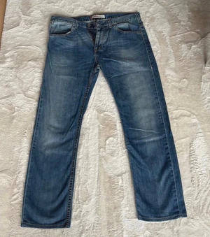 Levi's 504 Straight blå jeans - Säljer ett par klassiska Levi's 504 Straight jeans i blå tvätt med snygga slitningar. Modellen har rak passform, fem fickor och knappgylf. Perfekta för dig som gillar en tidlös look och vill ha jeans som sitter skönt hela dagen.