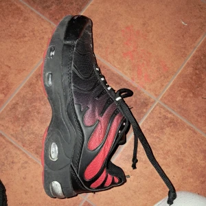 Svarta och röda sneakers med snörning - Säljer ett par feta sneakers i svart och rött med coola detaljer och snörning. Skorna har en chunky sula med synliga luftbubblor och meshpartier för extra andningsförmåga. Snygg färgövergång från svart till rött på sidorna och mönstrade skosnören.