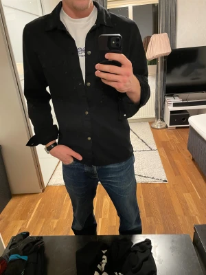 Overshirt från Zara - Svart overshirt från Zara i storlek L. Snygg och stilren med klassisk krage, två bröstfickor och tryckknappar framtill. Relativt robust och skön att ha på sig, funkar perfekt att kombinera med tisha eller skjorta. Priset är ej hugget i sten!