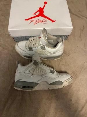 Nike Air Jordan 4 White Cement - Nike Air Jordan 4 White Cement med vit ovandel i skinn och mesh, grå detaljer med stänk och röda Jumpman-loggor på plösen. Klassisk siluett med snörning och synlig Air-enhet i sulan. Perfekta för dig som gillar retrostil och streetwear.