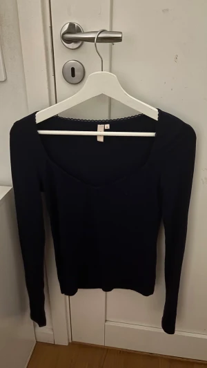 Blå långärmad topp med v-ringning - Säljer en stilren blå långärmad topp i storlek S. Toppen har en snygg v-ringning och diskret spetskant runt halsen som ger en extra touch. Perfekt att matcha med jeans eller kjol för en clean look.