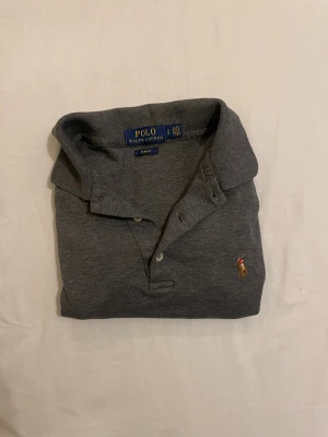 Grå pikétröja från Polo Ralph Lauren - Säljer en jätte snygg piké ifrån Ralph Lauren. Den är i toppen skick men har ett litet hål. Skriv till mig vid intresse❤️ 