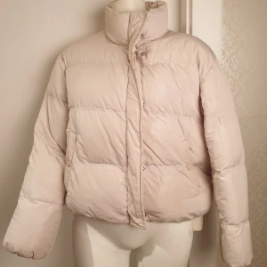 Babyrosa Pufferjacka - Säljer en stilren ljusrosa pufferjacka med hög krage och knappar. Jackan har en pufferdesign som ger en skön och varm känsla. Perfekt för kyliga dagar. ❗Har sminkfläck vid kragen och behöver tvättas, därav priset.