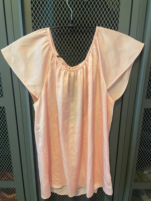 Ljusrosa blus från Forever 21 - Söt ljusrosa blus från Forever 21 med vida, korta ärmar och rundad halsringning. Blusen har ett lätt glansigt tyg och en snygg öppen detalj i ryggen med knapp. Perfekt för dig som gillar en luftig och feminin stil.