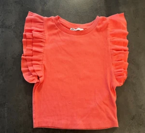 Rosa och svart volangtopp från Zara - Två croppade toppar från Zara, en i stark rosa och en i svart. Båda har korta ärmar med breda volanger som ger en cool och trendig look. Materialet är mjukt och ribbat, perfekt för att lyfta din outfit med lite extra edge. Båda topparna är i storlek S men sitter som XS💕