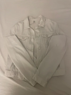 Vit jeansjacka  - Snygg vit jeansjacka från &Denim i klassisk modell med krage, knappar framtill och två bröstfickor. Jackan har raka, långärmade ärmar och är tillverkad i slitstarkt bomullsmaterial. Perfekt för dig som gillar clean och enkel stil.