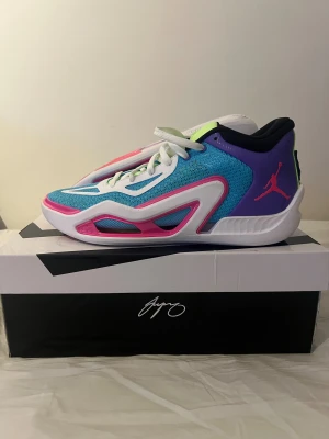 Jordan JT sneakers i blå och rosa - Säljer ett par färgstarka Jordan JT sneakers med mesh-överdel i blått, detaljer i vitt och neonrosa samt lila hälparti med rosa Jumpman-logga. Tungan är limegrön med JT-tryck och palmträd. Sulan är vit med rosa och lime detaljer, och skorna har snörning för perfekt passform.