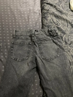 Grå jeans med dubbla knappar - Säljer ett par grå jeans från ginatricot young med snygg tvättad look. Byxorna har dubbla knappar i midjan, klassiska fem fickor och bälteshällor. Perfekta för dig som gillar en avslappnad men ändå stilren vibe.