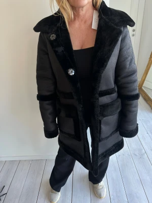 Svart lång pälsjacka  - Snygg svart lång pälsjacka med bred krage och markerade kanter i päls. Perfekt för dig som vill ha en statementjacka med lyxig känsla. 😍😍 Pris kan diskuteras.